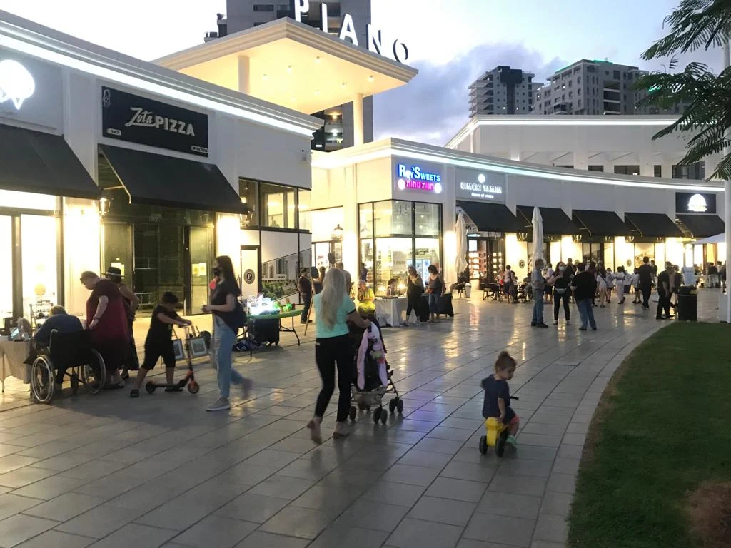 People walking through Piano Plaza in Ir Yamim at dusk